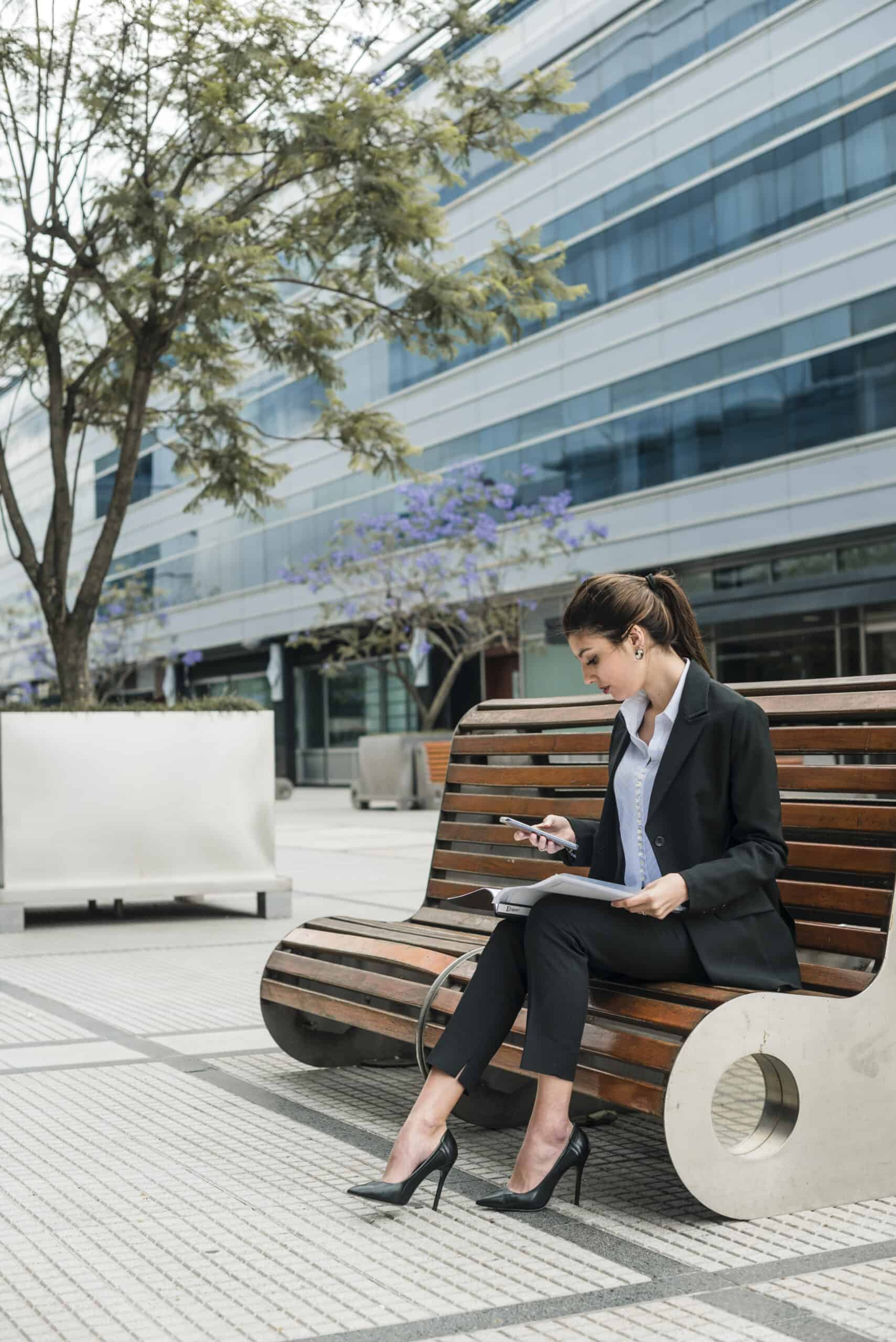 young-businesswoman-sitting-outside-building-looking-mobile-phone